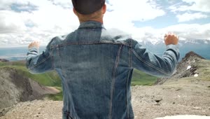 Download Stock Video Man In Denim Jacket Raises Arms To Mountain Landscape Animated Wallpaper