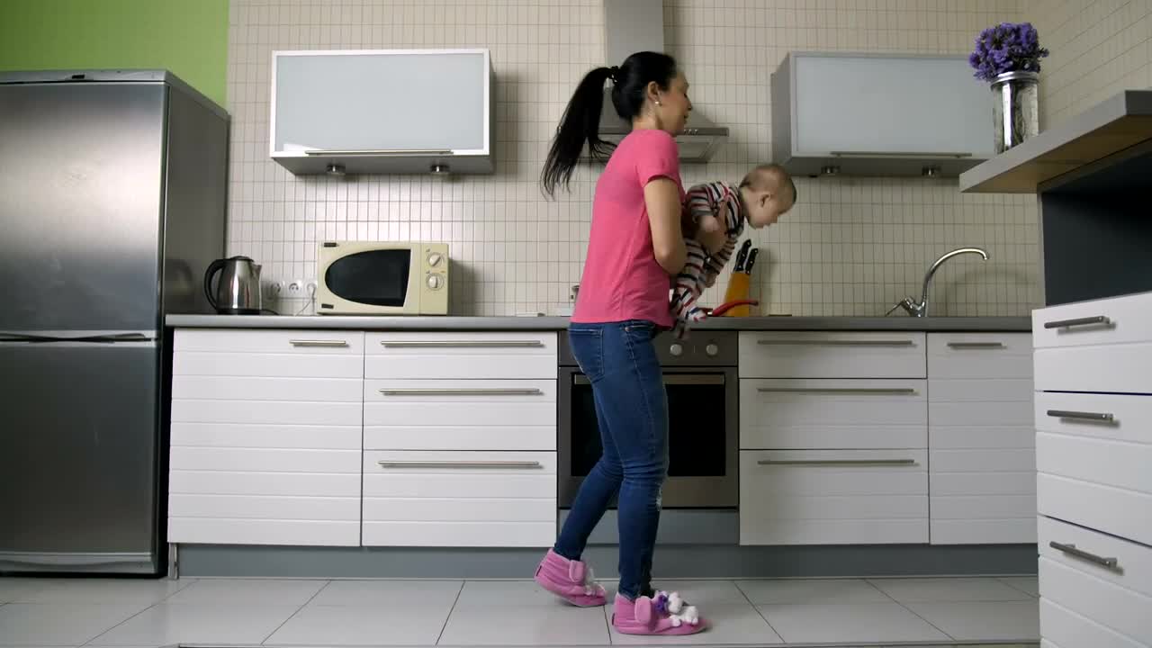 Download Free Stock Video Young Woman Cooking In A Kitchen Carrying Her Baby Live Wallpaper